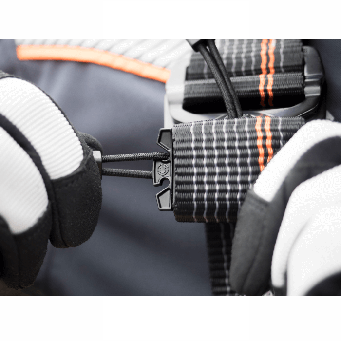 Skylotec ignite trion sicherheitsgurt mit schwarz orange kariertem gurtband und schwarzer metallschnalle wird von hand mit handschuh eingestellt