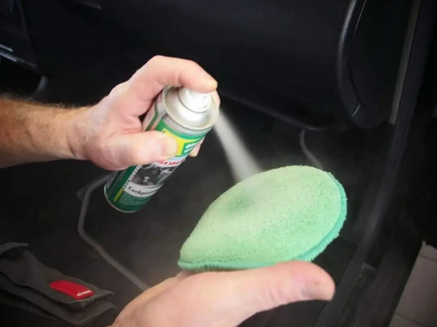 Grüner mikrofaser-autopflegeschwamm wird mit sonax cockpitpfleger 400ml reinigungslösung eingesprüht