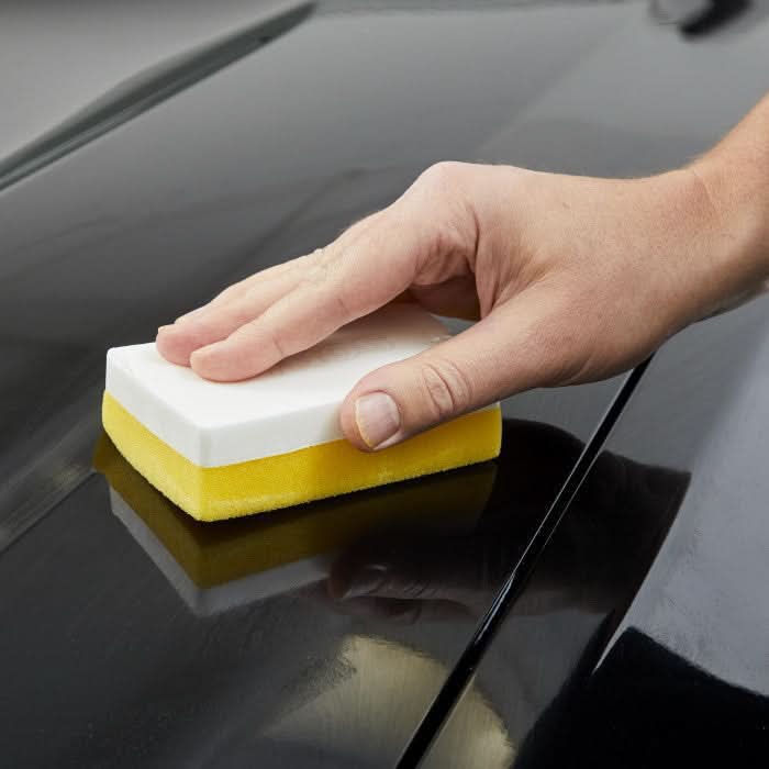 Gelb weißer zweifarbiger rechteckiger sonax applikationsschwamm zum polieren der oberfläche eines autos