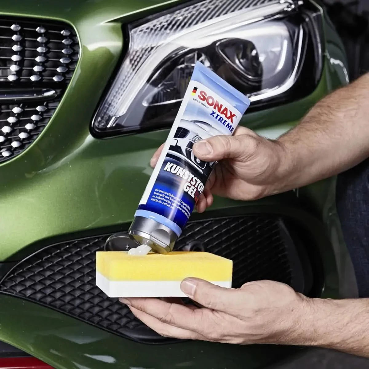 Ein tubus sonax xtreme kunststoffgel außen nanopro 250ml mit blau-silbernem etikett wird auf einen gelben schwamm gedrückt