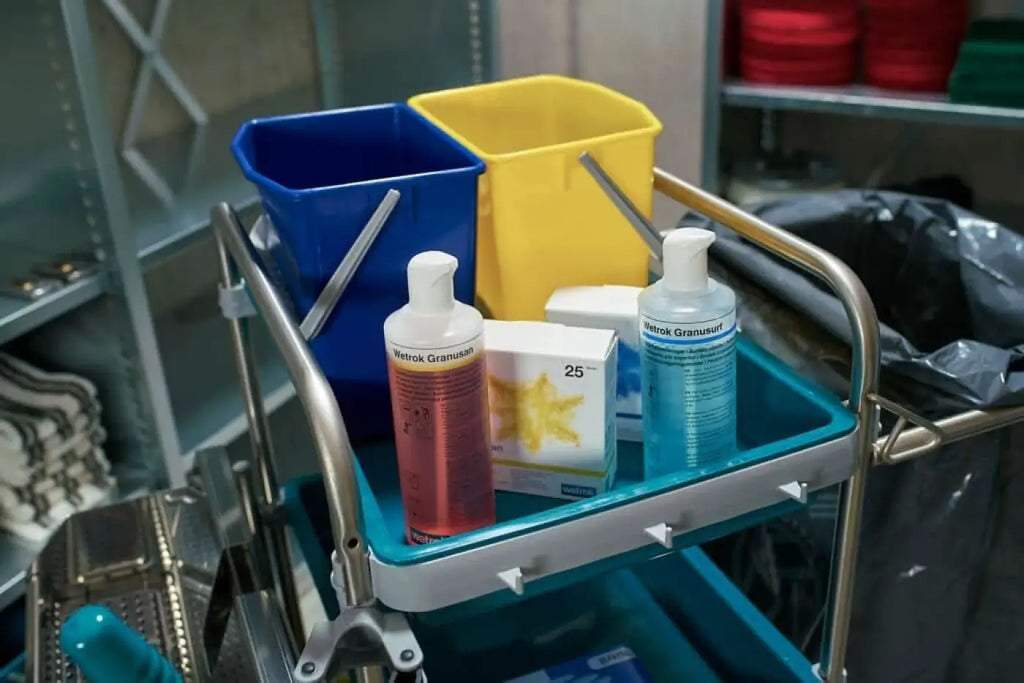 Blaue und gelbe plastikeimer mit metallgriffen neben wetrok granuusan desinfektionsmitteln auf medizinwagen