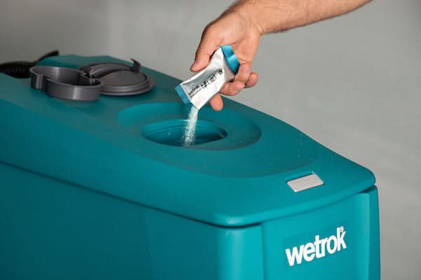 Eine hand schüttet weißes pulver aus einem blau-silbernen beutel in eine türkise wetrok reinigungsmaschine
